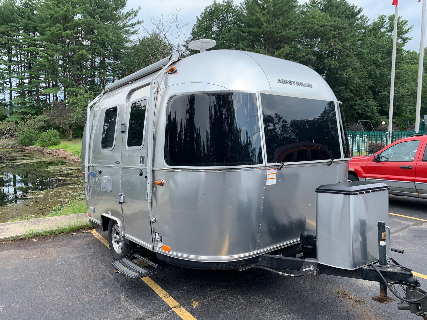 Airstream RV rental: Silver travel trailer, parked by a pond with tall trees. Perfect for your next adventure.