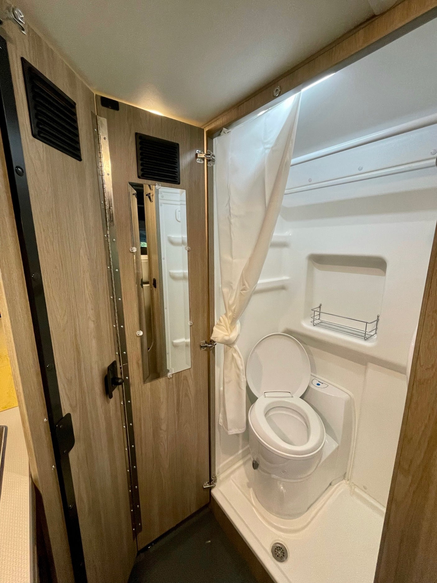 RV rental's compact wet bath showing toilet, shower, mirror. Efficient design for travel.
