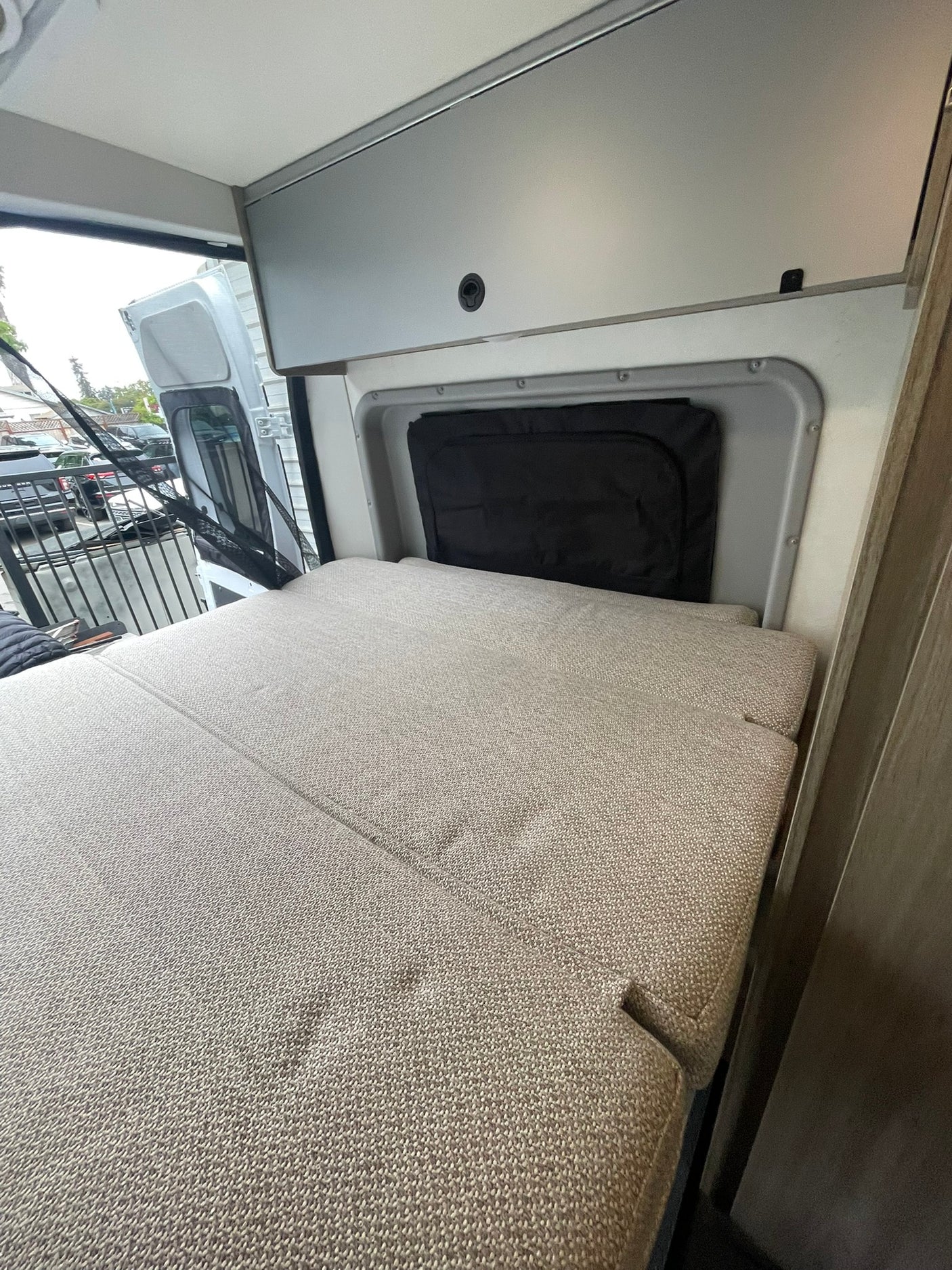 Cozy RV rental interior with a bed, overhead cabinets, and open rear doors, ready for travel.