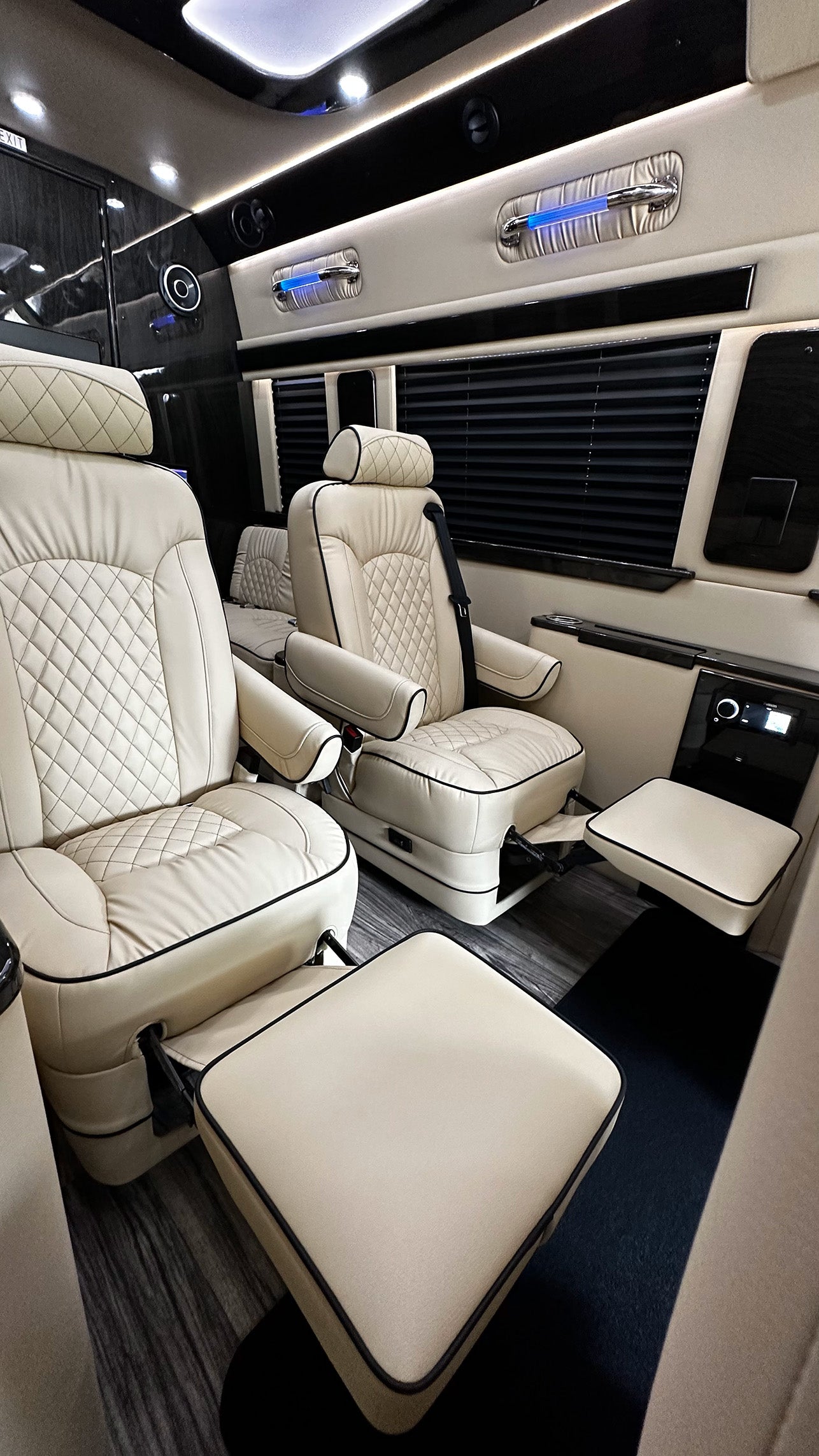 Luxurious RV rental interior with cream quilted captain's chairs, adjustable footrests, ambient lighting, and privacy blinds.
