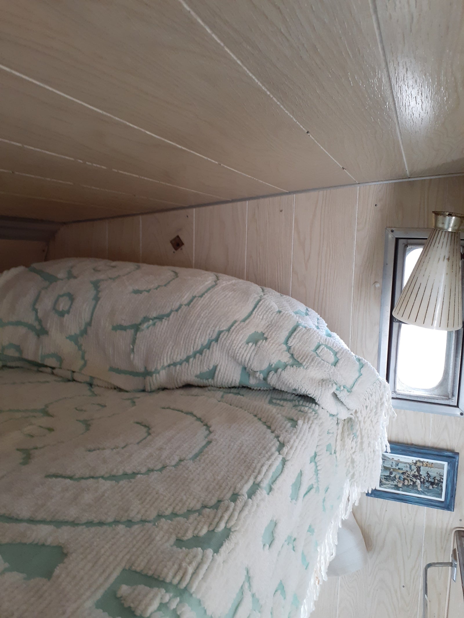 Inside an RV rental: light wood walls, a window, and a white and teal patterned blanket create a cozy interior scene.
