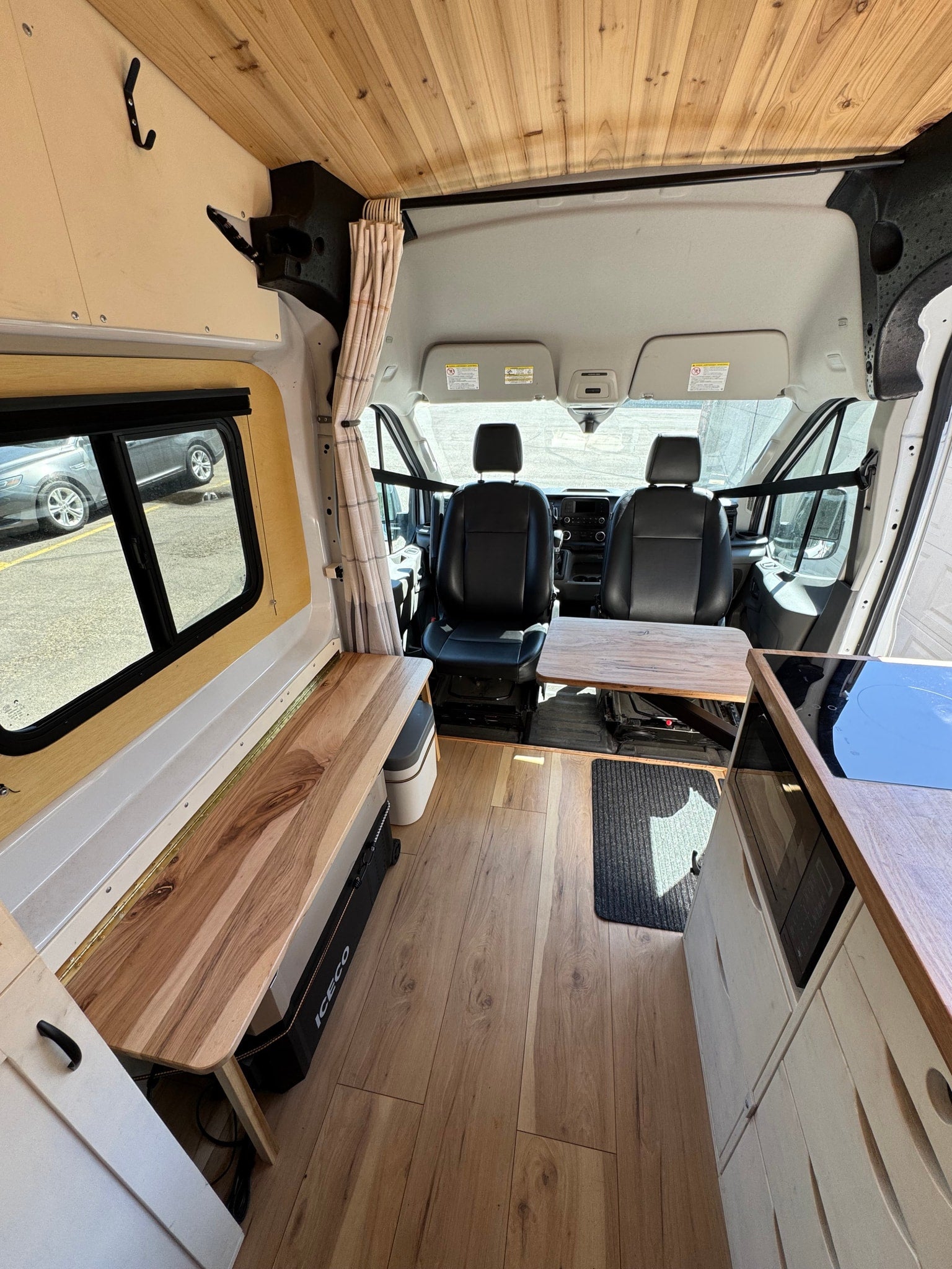 This RV rental camper van interior showcases a wooden ceiling, wood flooring, kitchen, bench seating, and front cabin access.