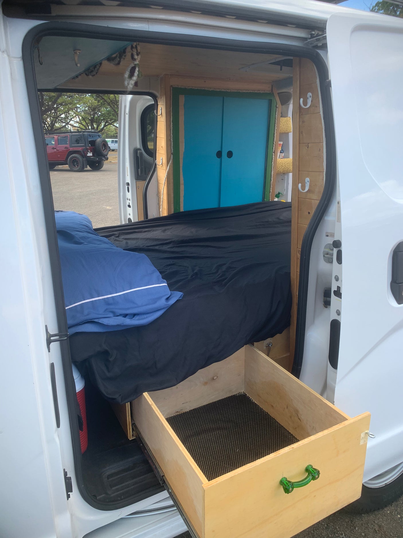 RV rental interior showcasing a compact camper bed, built-in wooden storage, and a vibrant blue cabinet.