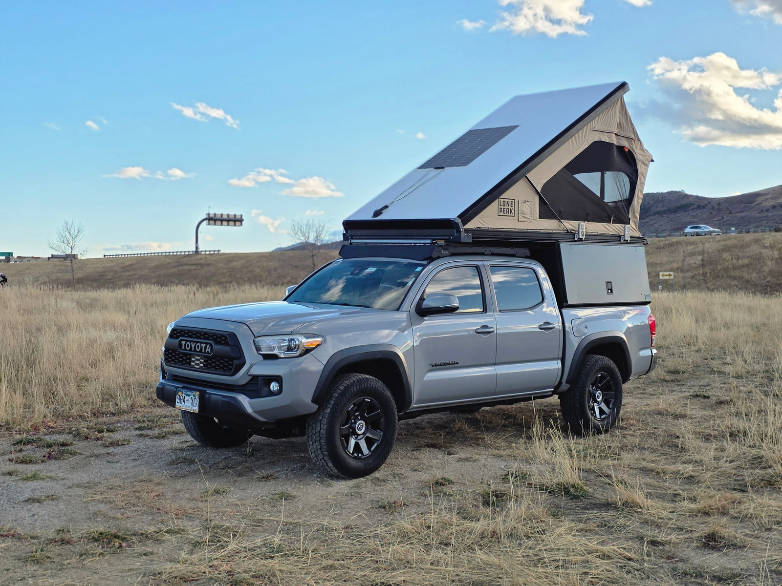 Custom Toyota Tacoma overlanding truck with a deployed pop-up camper and solar panel, ideal for an rv rental adventure.