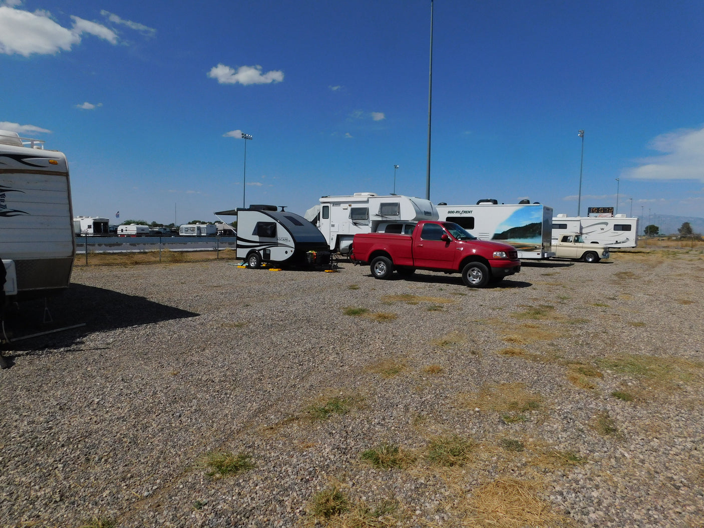 RV rental unit, a small teardrop camper, and a red pickup truck parked among other RVs on a sunny gravel lot.