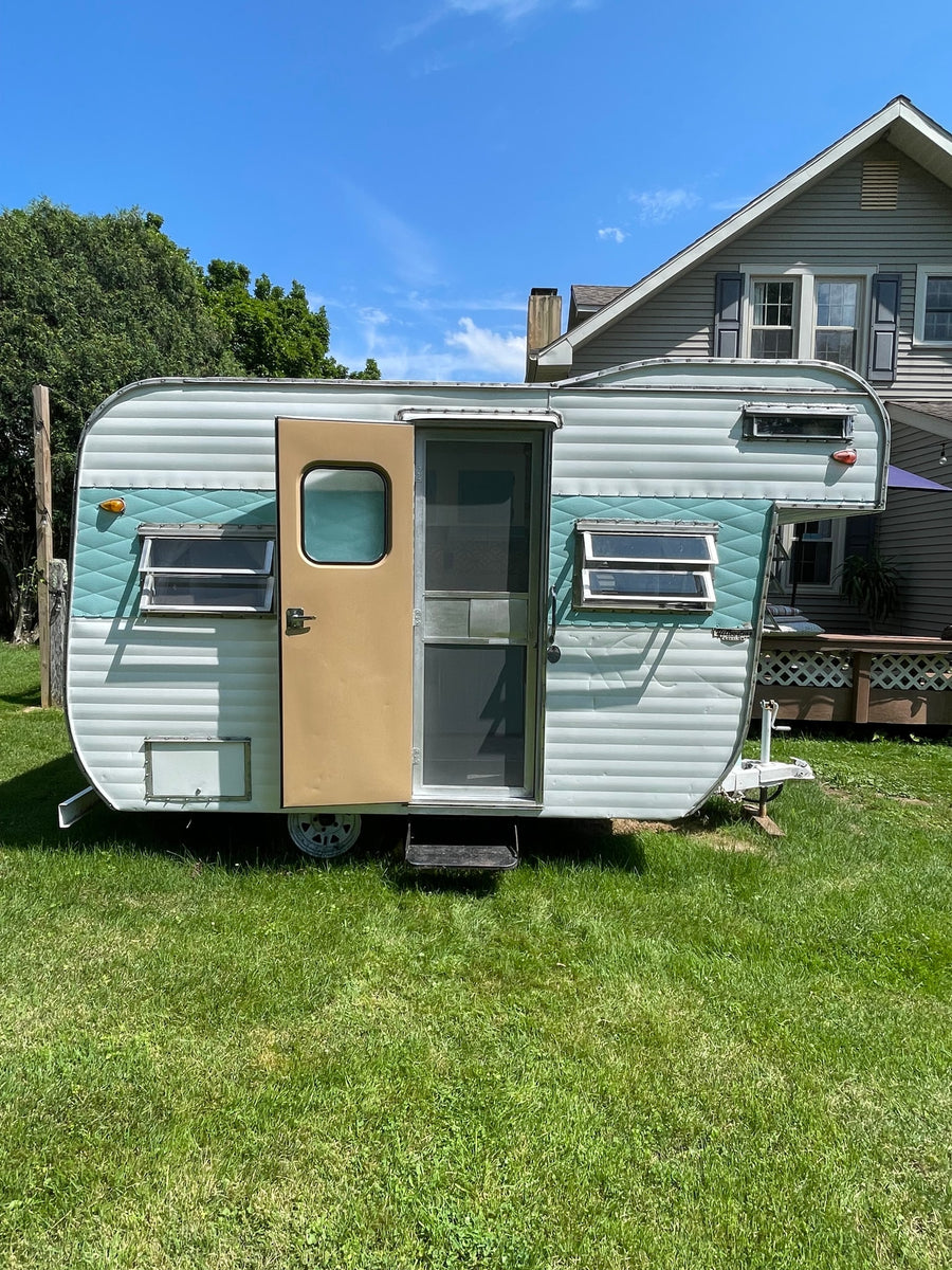 seen at dusk. Perfect for an RV rental or camping adventure.|Vintage light blue camper parked on green grass