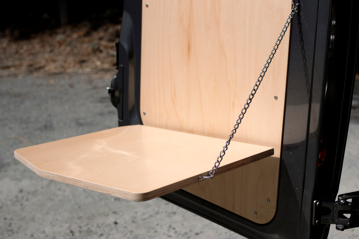 Fold-down plywood table on an RV rental, securely supported by a chain, perfect for convenient outdoor use.