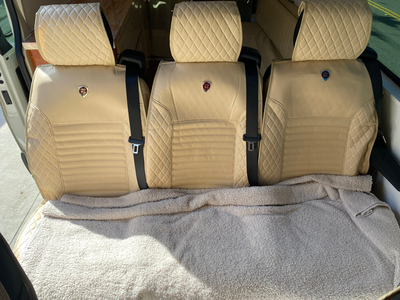 Light-colored, quilted RV rental seats with seatbelts, covered by a soft blanket. Ready for comfortable and stylish travel.