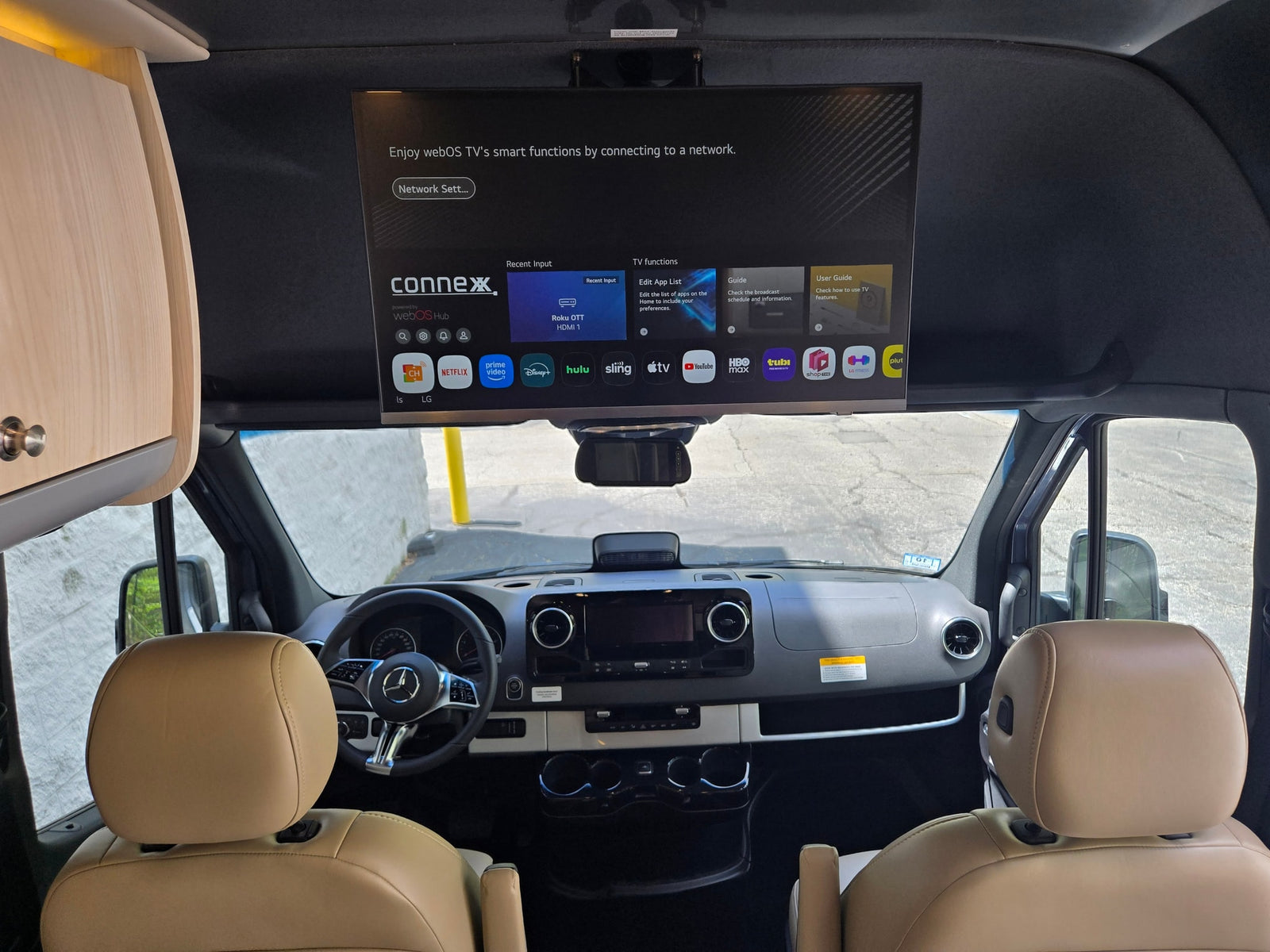 A modern RV rental's front cabin, featuring a large overhead smart TV with streaming apps like Netflix and a sleek dashboard.