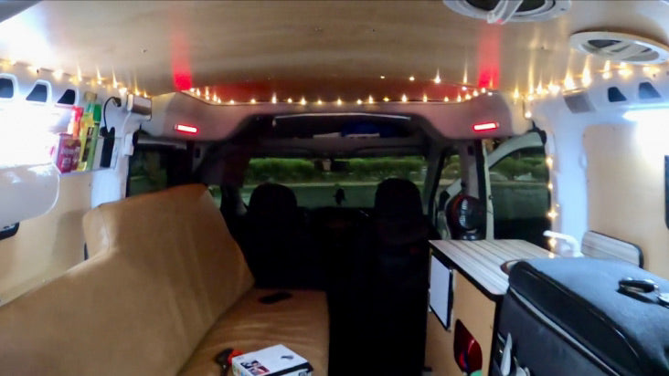 Cozy RV rental camper van interior: string lights illuminate a comfy bed, small table, and storage.