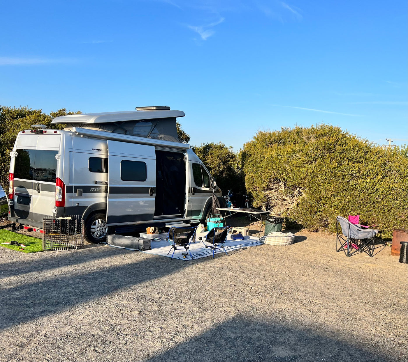 ideal for secluded nature camping.|Silver RV rental camper van parked on a gravel lot. A person is inside. Scenic trees — photo 8