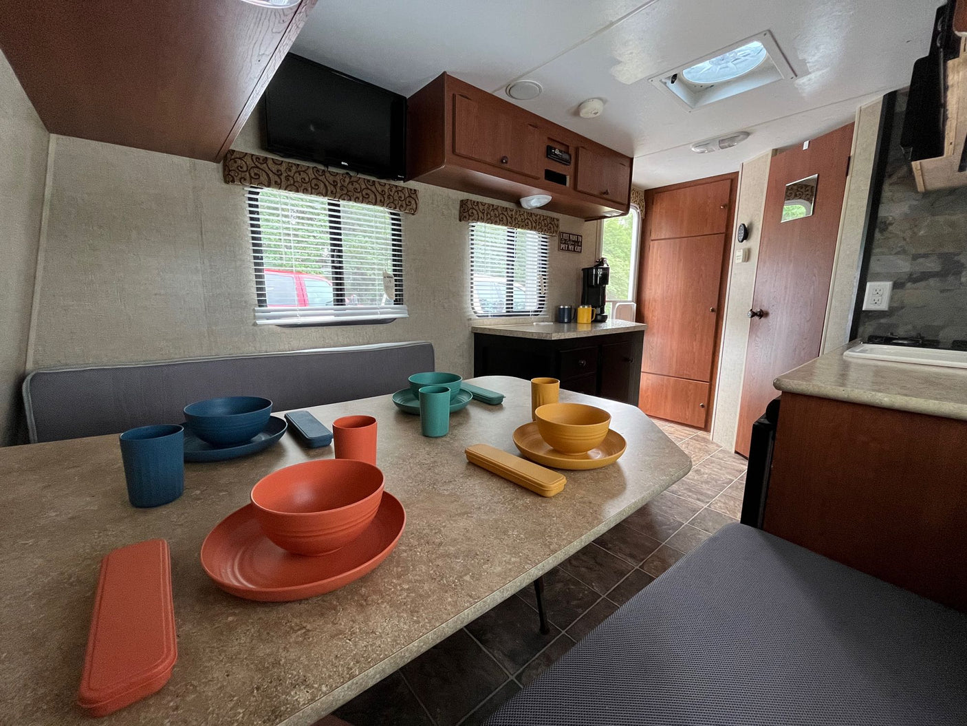 facing a colorful dinette on right. Ideal for travel.|Step into this RV rental: a compact interior features a dining table with colorful tableware