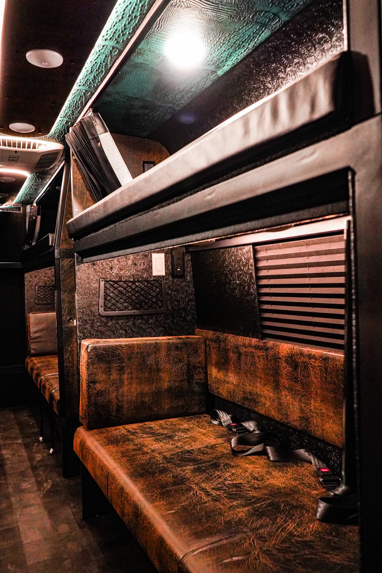 Luxurious custom RV rental interior with distressed brown seating, textured walls, and overhead bunks.