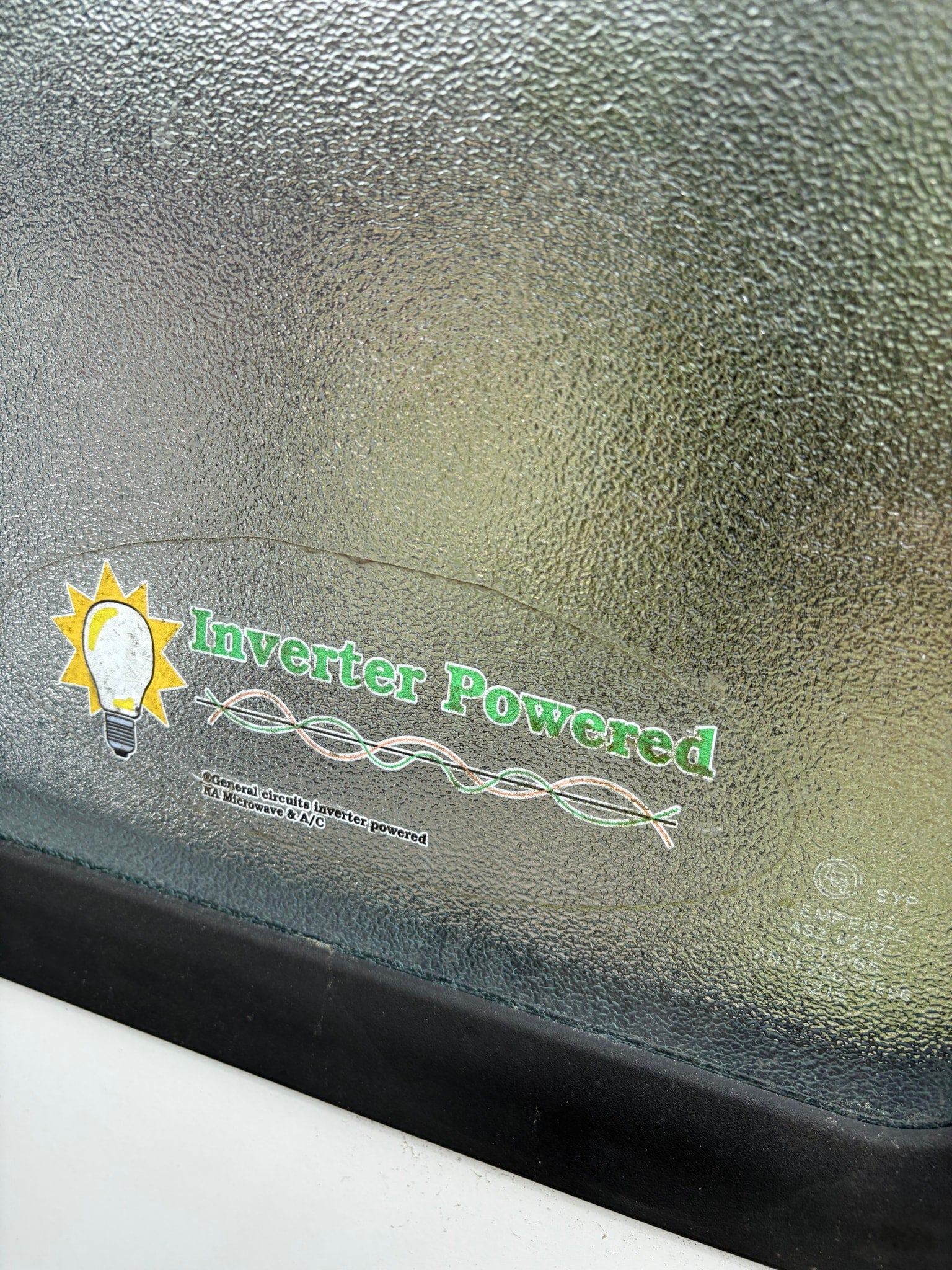 Sticker on an RV rental's textured window announces 'Inverter Powered' for general circuits, microwave, & A/C.