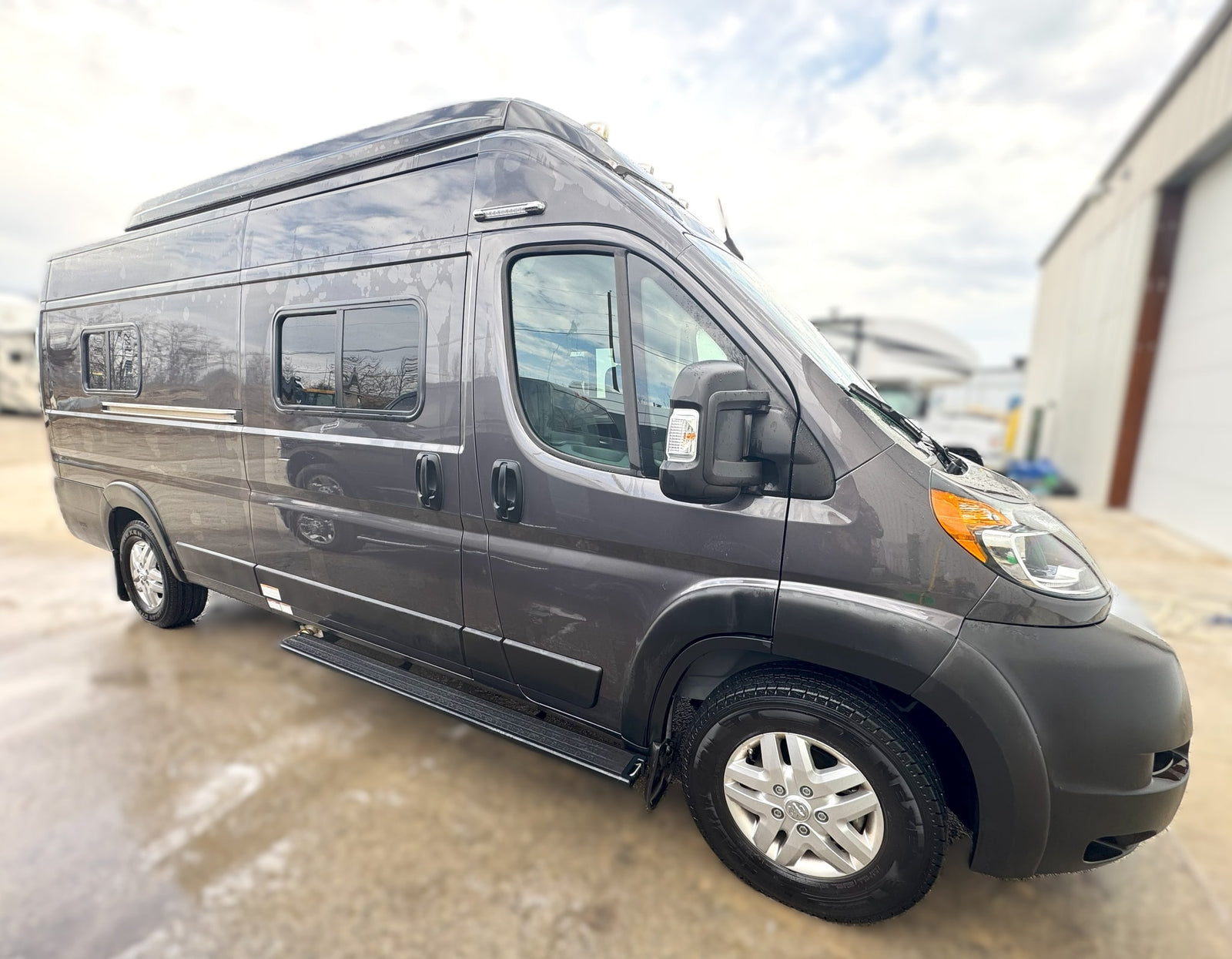 Dark gray camper van RV rental, side view. Features include multiple windows, silver wheels, and a running board.