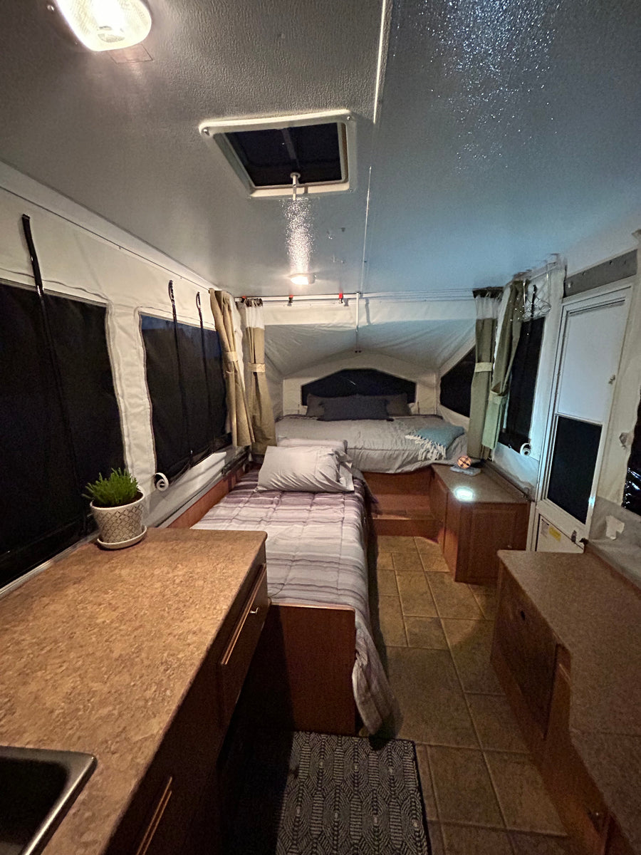 Inside a comfortable RV rental: two beds, tiled floor, and a compact kitchen counter. Ready for adventure!