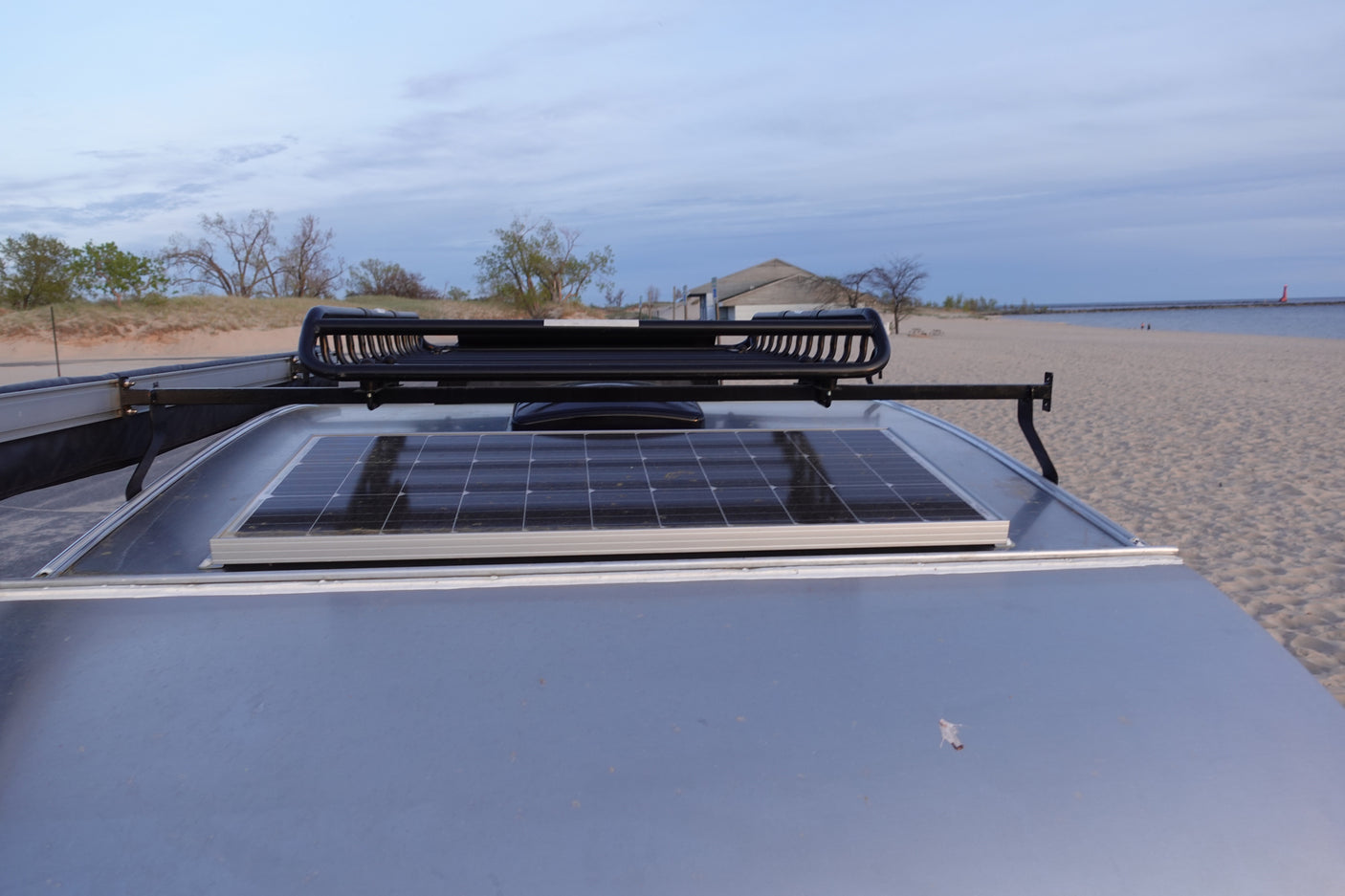 RV rental with solar panel & roof rack at a sandy beach. Ideal for off-grid travel & outdoor adventures.
