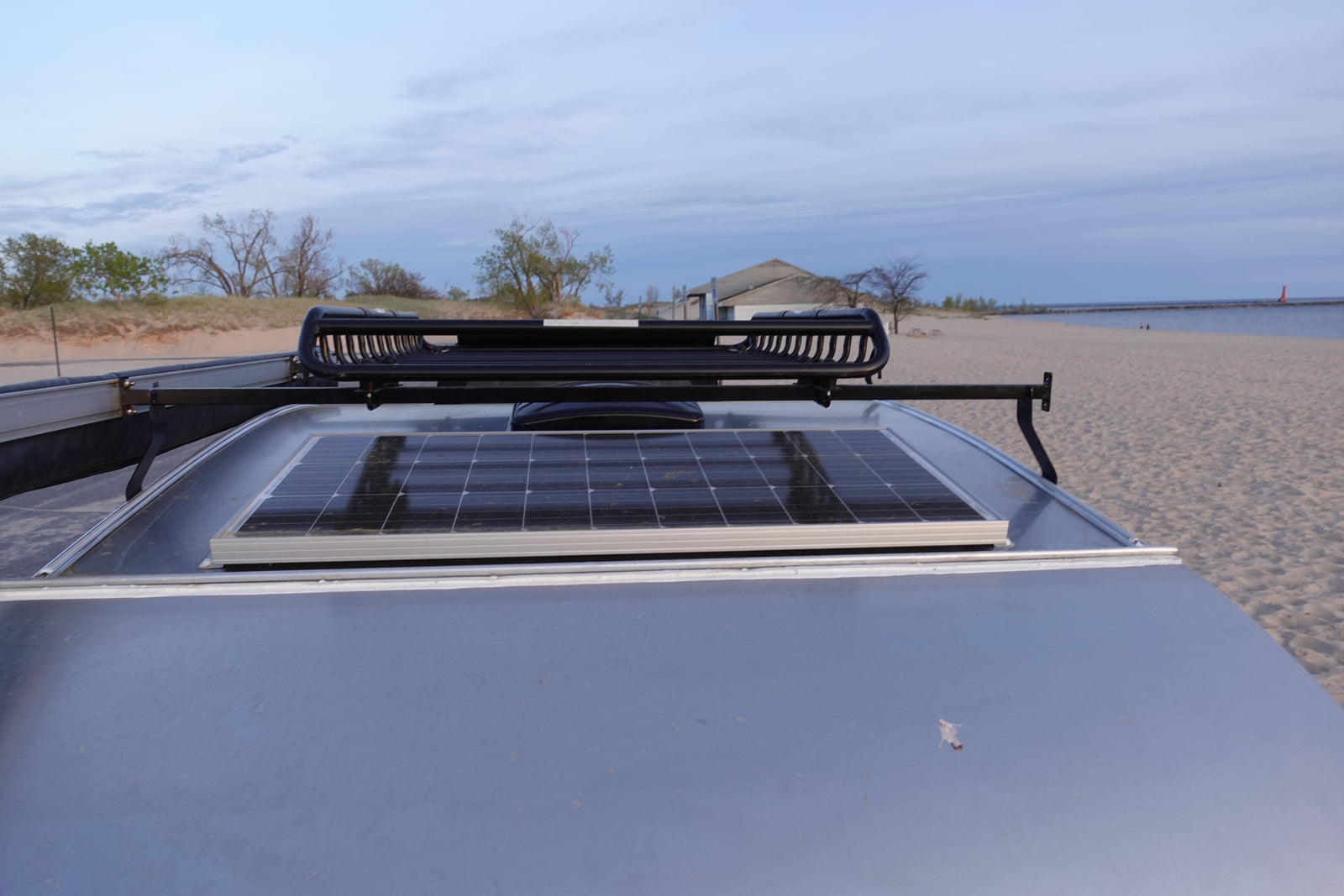 RV rental with solar panel & roof rack at a sandy beach. Ideal for off-grid travel & outdoor adventures.