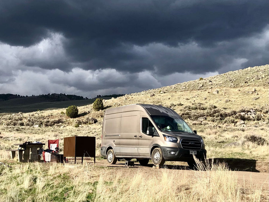 RV rental: A tan camper van parked on a dirt road with a picnic setup