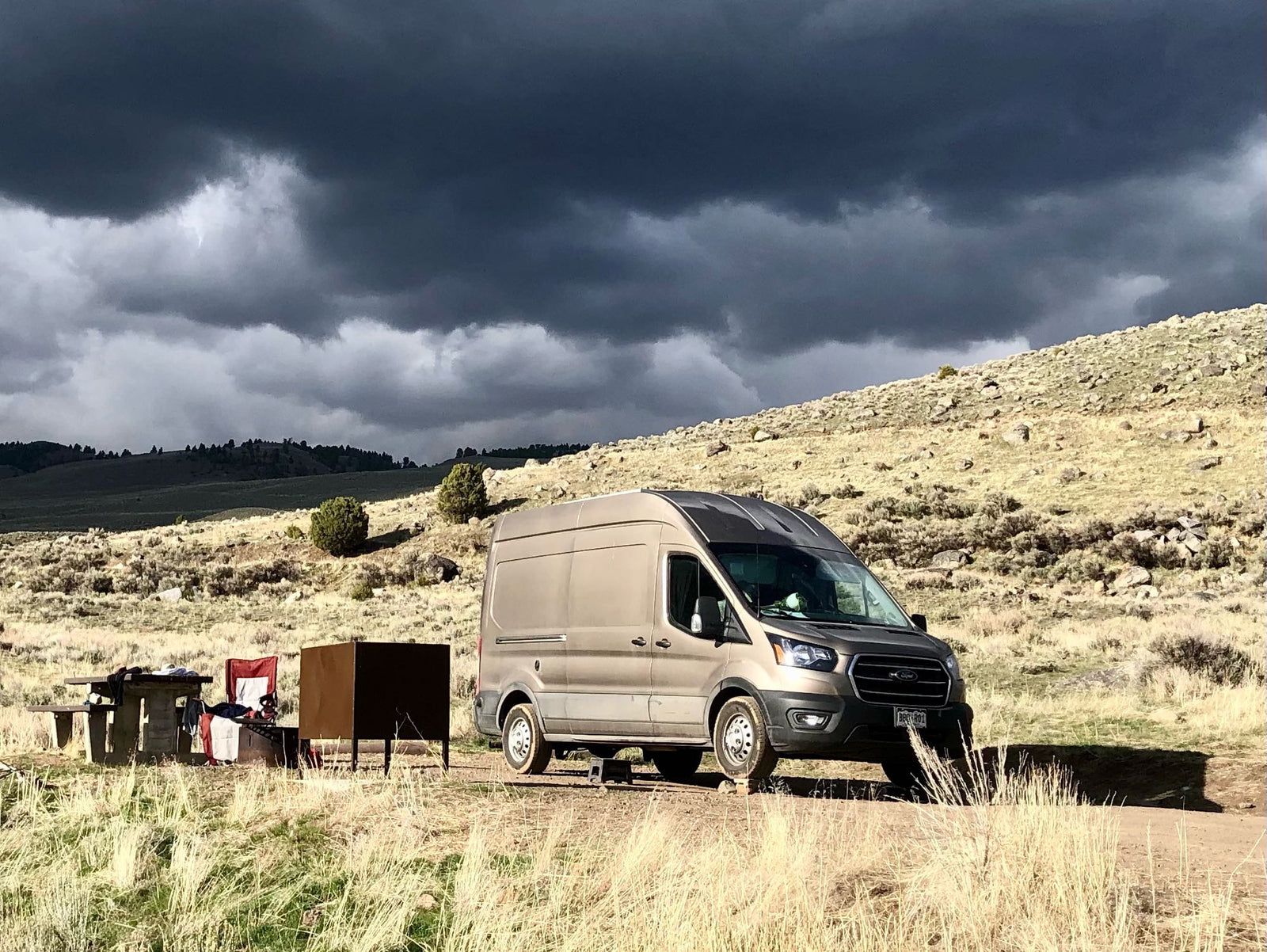 RV rental: A tan camper van parked on a dirt road with a picnic setup