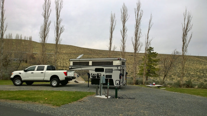 and a set dining table with flowers on green grass under trees.|A white truck with a Palomino RV rental and two bicycles on a rack