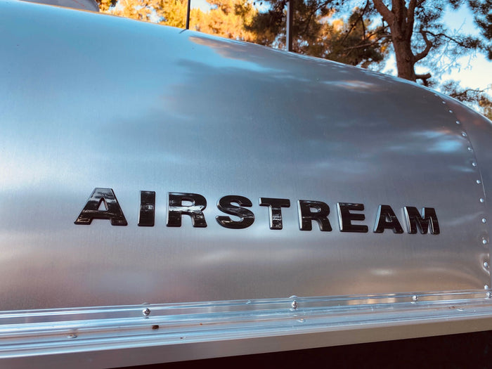 Close-up of an iconic silver Airstream travel trailer with its black logo, highlighting its polished metal and rivets. Great for RV rental.