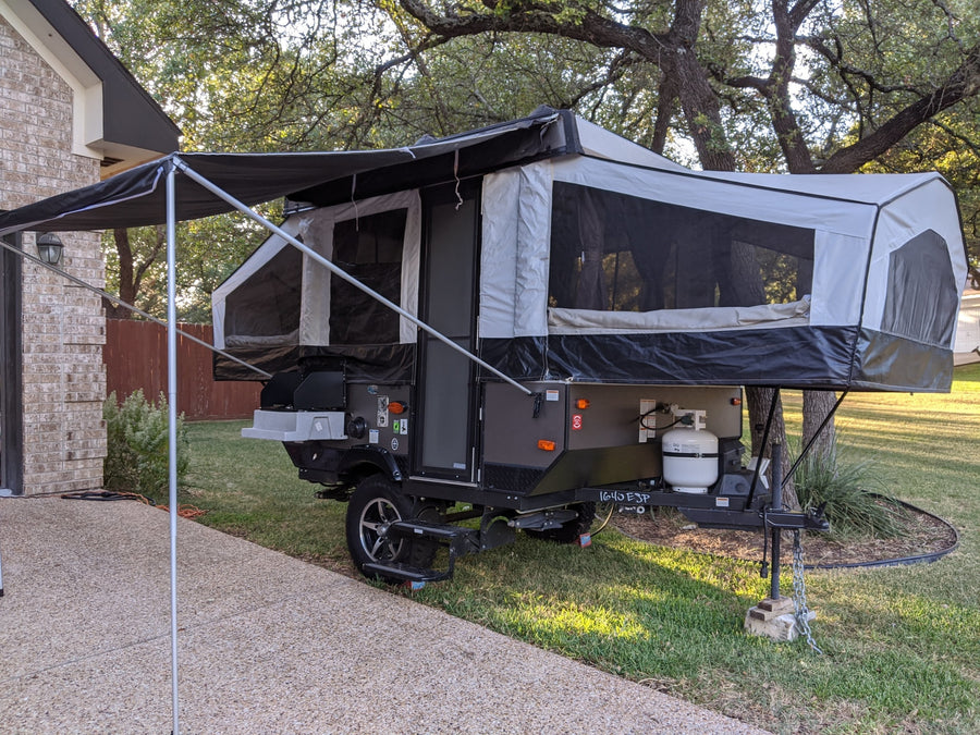 A pop-up camper, fully extended with an awning, parked on grass beside a brick house. Perfect for your next RV rental camping adventure.