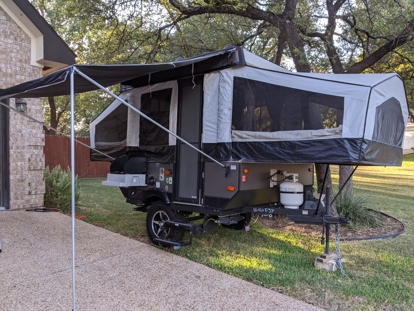 A pop-up camper, fully extended with an awning, parked on grass beside a brick house. Perfect for your next RV rental camping adventure.