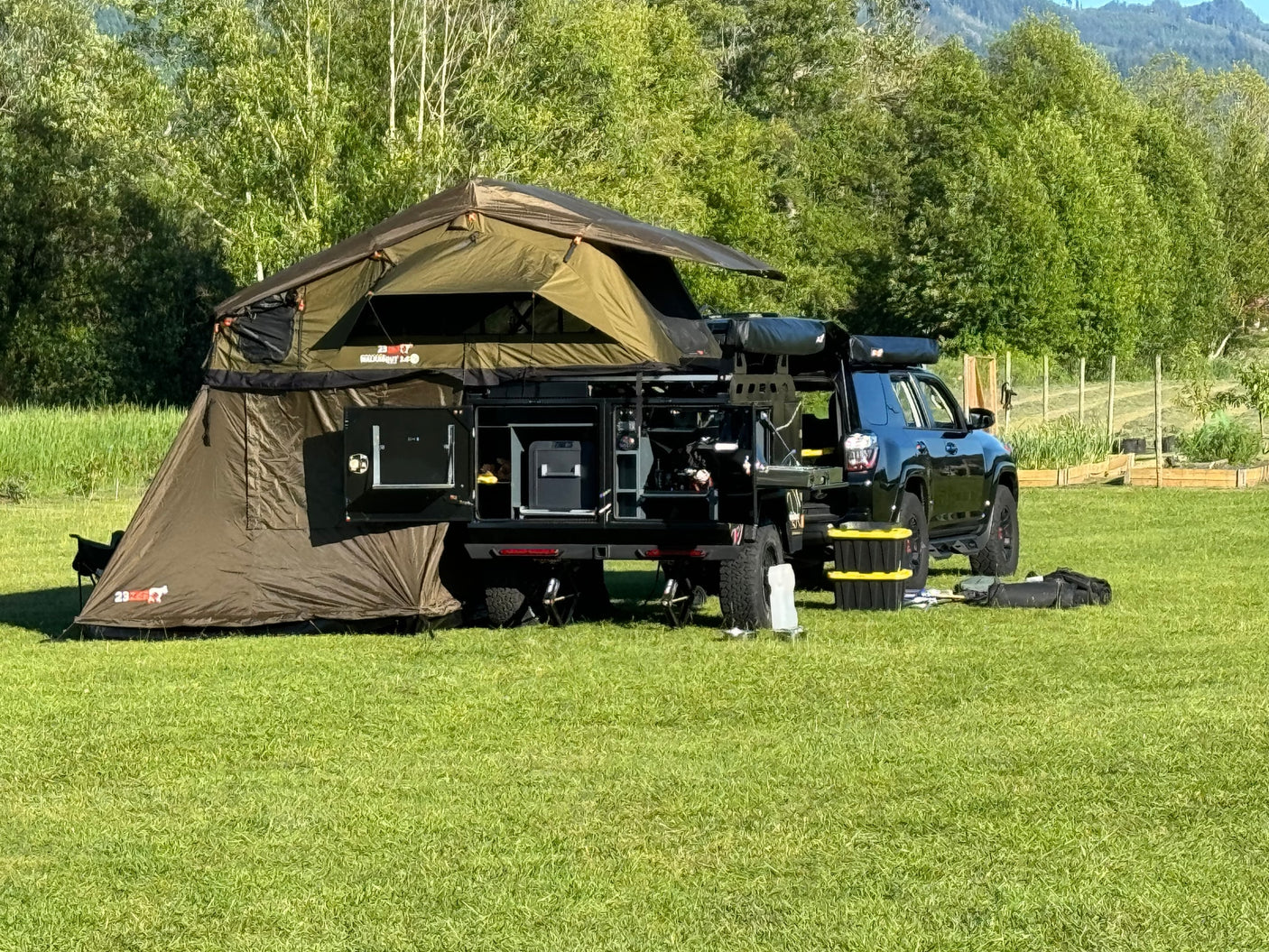 Black overlanding SUV with large roof-top tent & ground annex on grassy field, ready for adventure. A unique RV rental option!