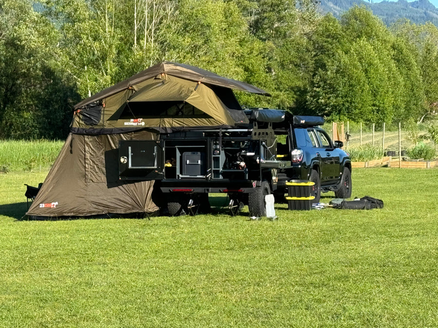 Black overlanding SUV with large roof-top tent & ground annex on grassy field, ready for adventure. A unique RV rental option!