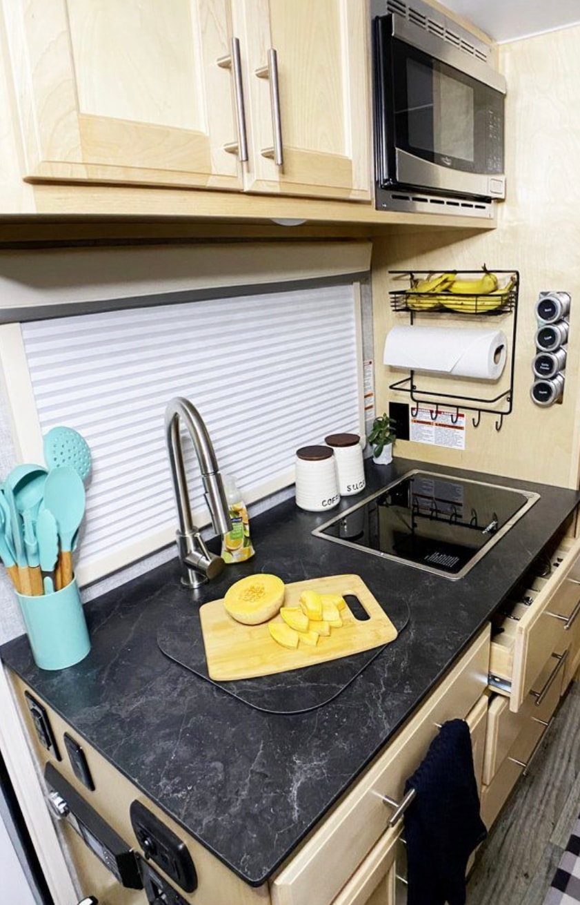 Explore a fully-equipped RV rental kitchen! Light wood cabinets, dark counters, sink, cooktop, & microwave offer home-like comfort.