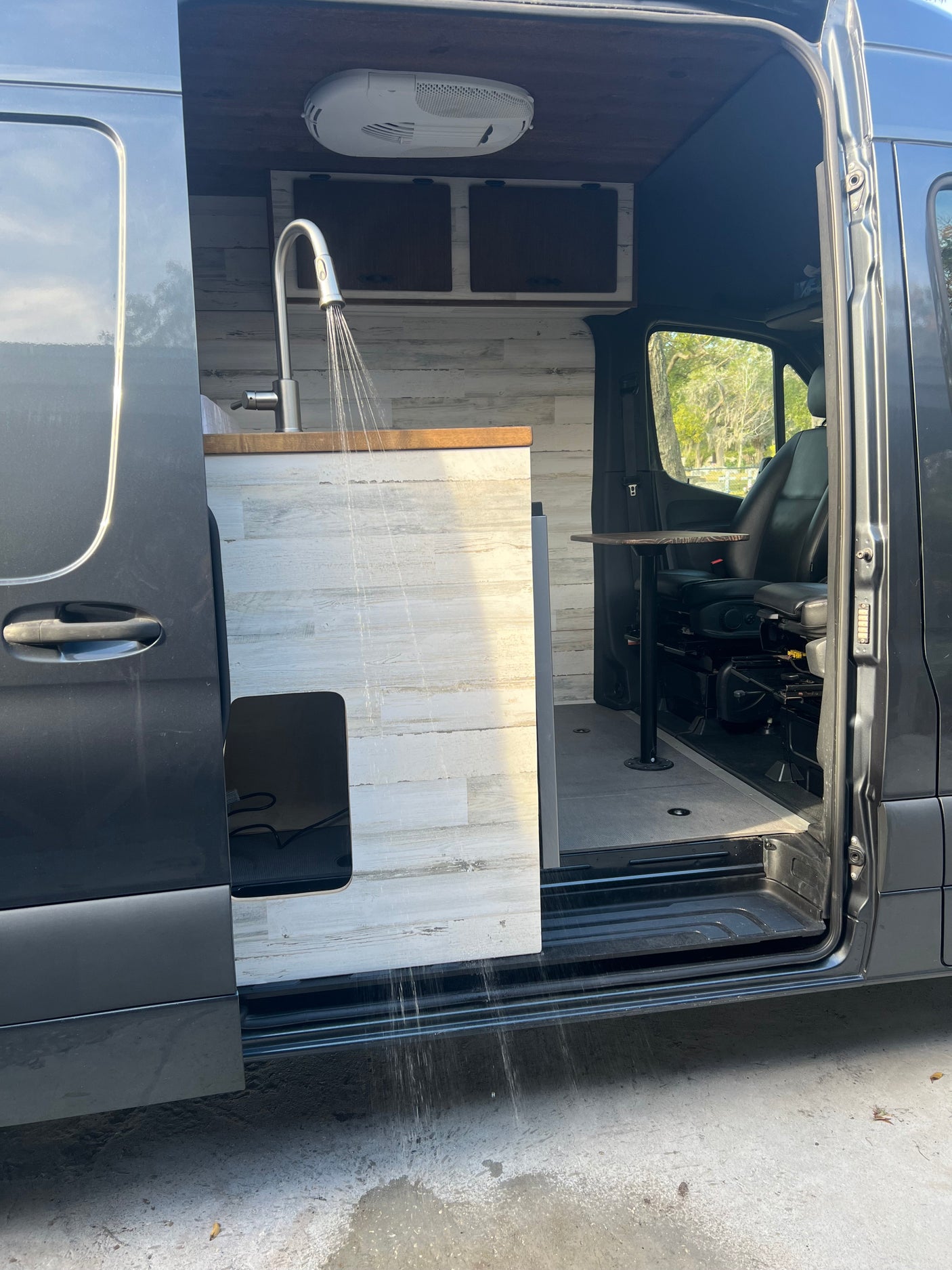 RV rental camper van interior. Sink with running water, wood countertops, and modern white plank walls.