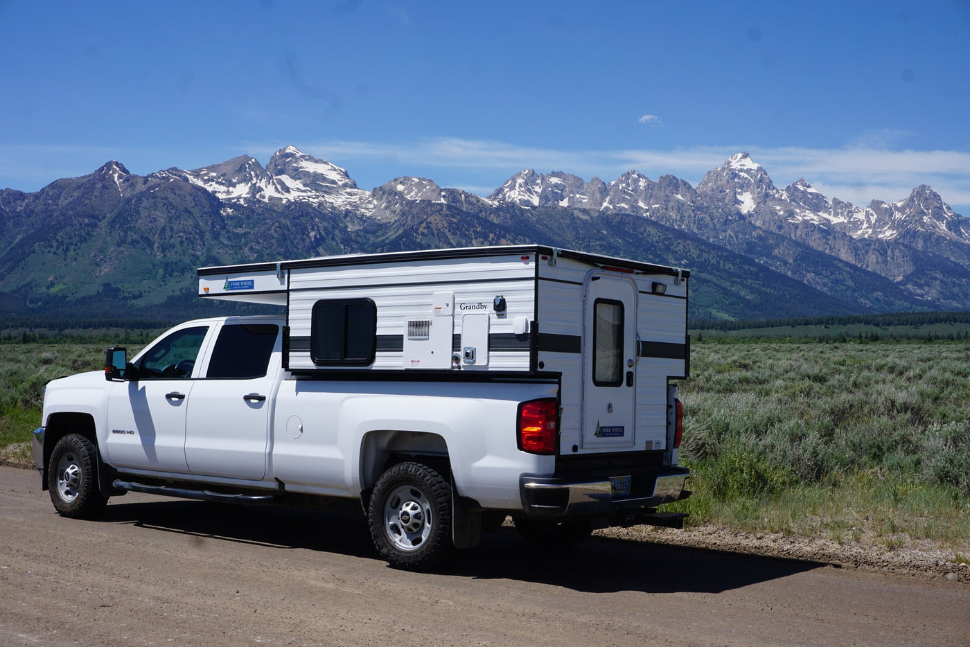 and entry door.|White Chevrolet 2500 HD RV rental truck camper with pop-up roof against mountains. Perfect for adventure camping.|RV rental: White truck with a Grandby Four Wheel camper on a scenic dirt road — photo 8