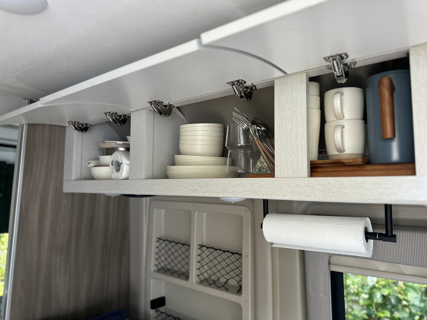 Organized overhead kitchen storage in an RV rental, featuring dishes, mugs, and a convenient paper towel holder.