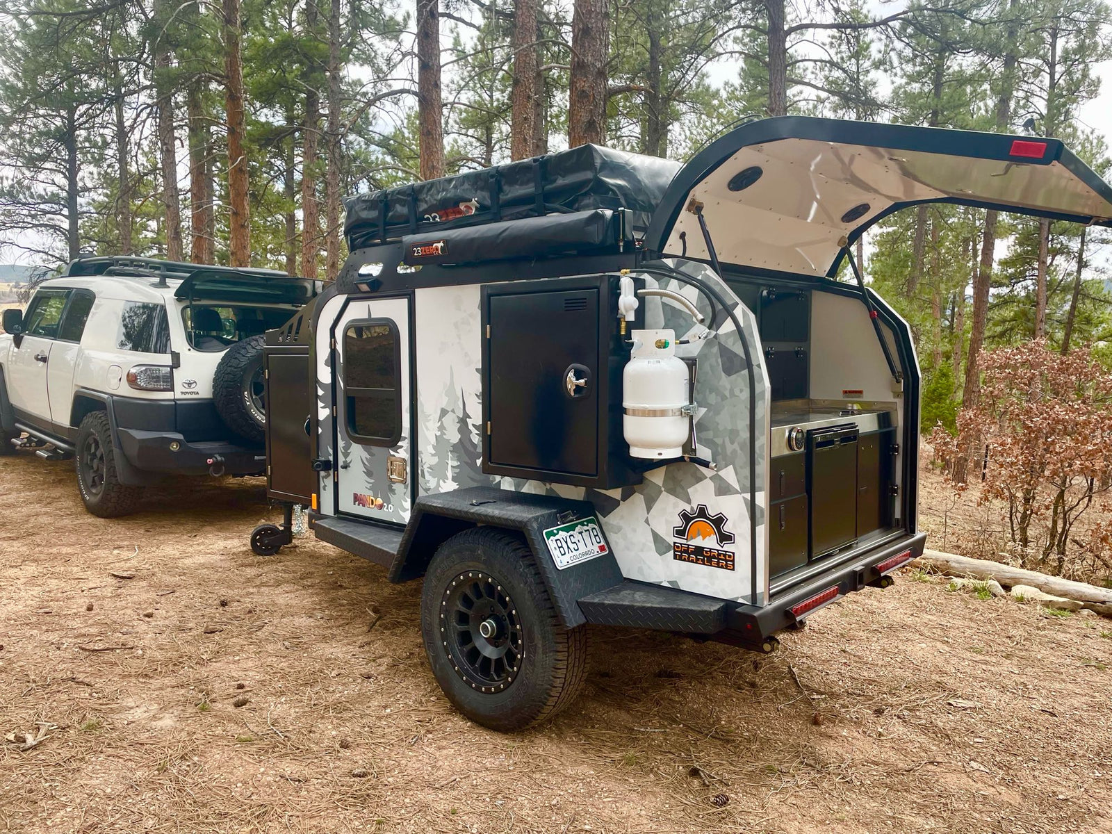 Off-grid RV rental: Toyota FJ Cruiser towing a camper trailer with an open outdoor kitchen and rooftop tent.
