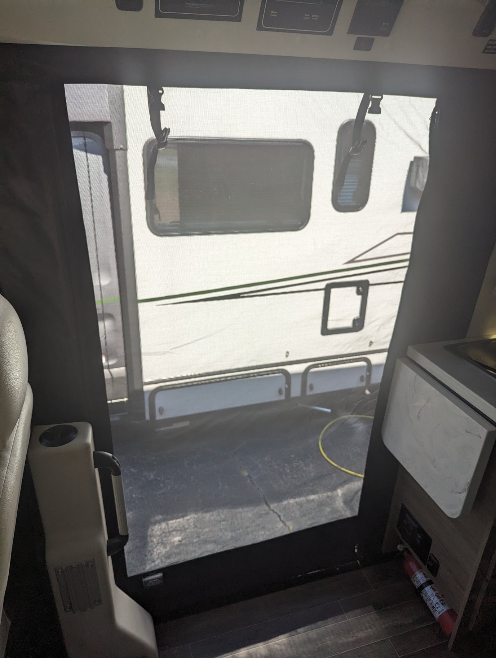 From an RV rental interior, a screen door shows a parked camper outside. Cabin controls are above, fire extinguisher below.