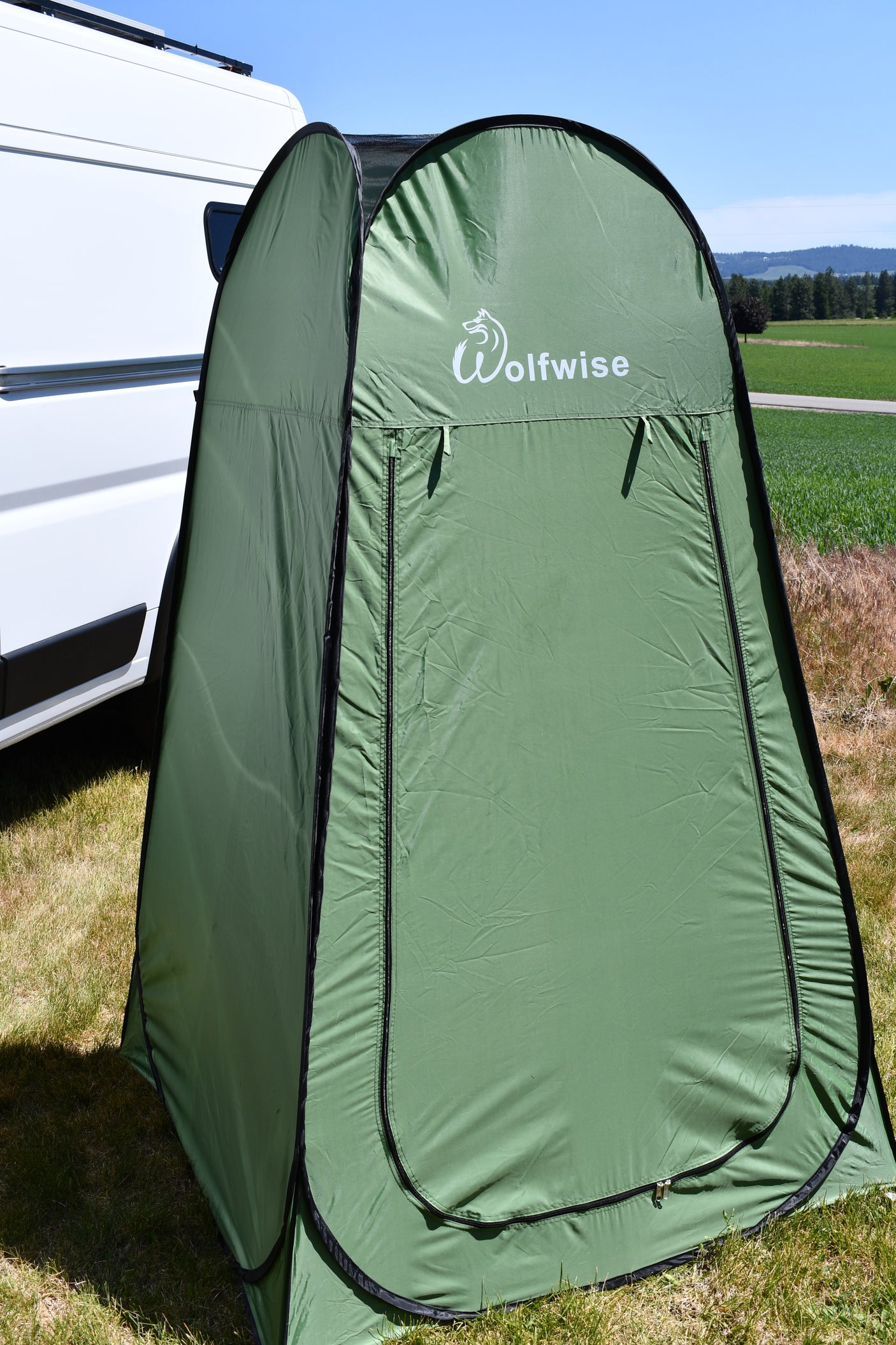 A green Wolfwise pop-up privacy tent set up next to a white RV, useful for any RV rental trip.
