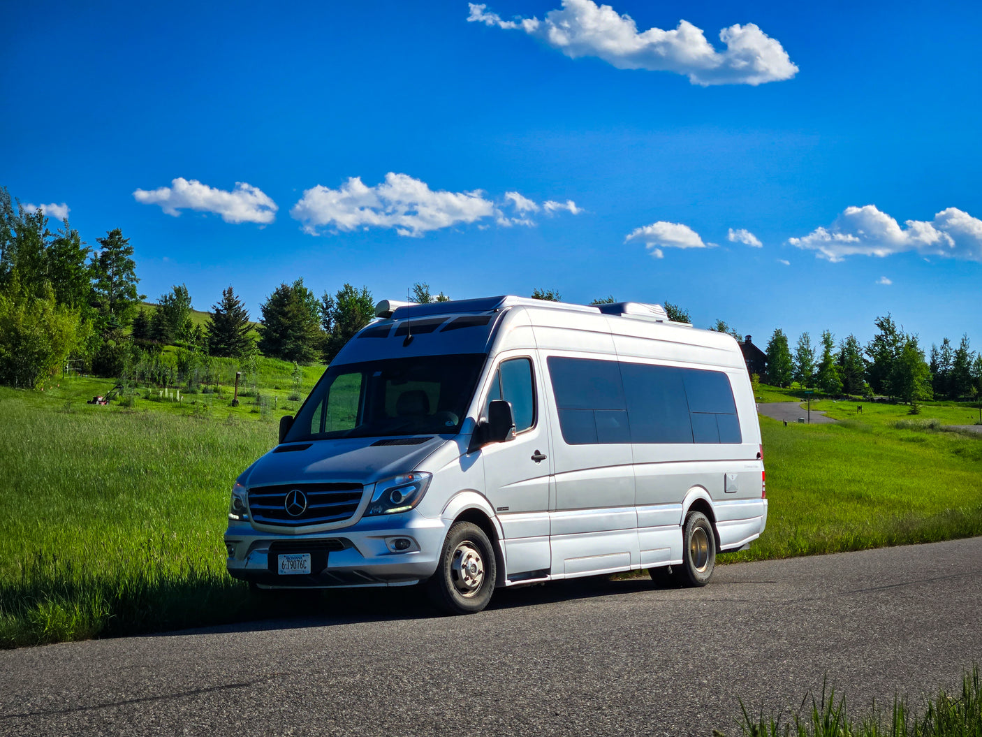 Silver Sprinter camper van, ready for your rv rental adventure, parked by green hills under a bright blue, cloudy sky.