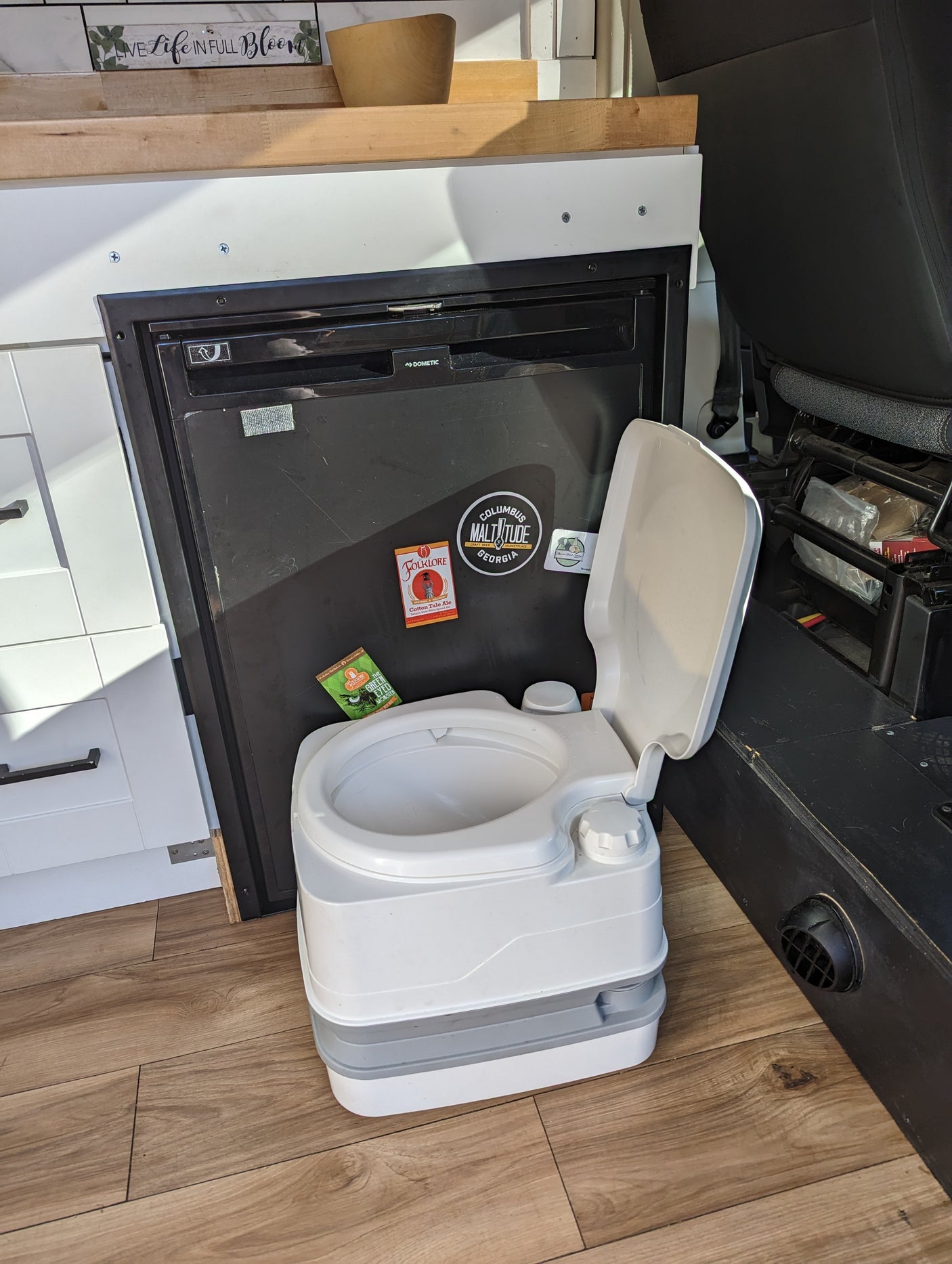 Practical rv rental interior: Dometic fridge with stickers, wood floors, and a portable toilet for off-grid travel.