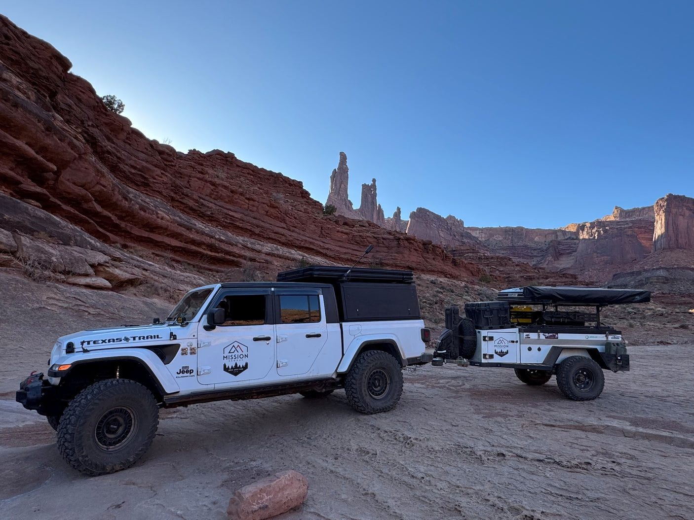 White Jeep Gladiator towing an overland camper trailer in red rock country. An ideal **RV rental** for off-road adventures!
