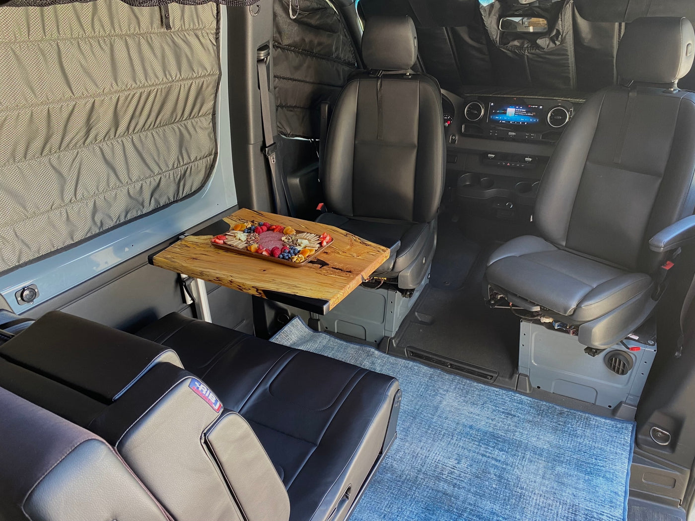 Experience comfortable dining in your RV rental! This van features swivel front seats, a rear bench, and a table with a charcuterie spread. — photo 11