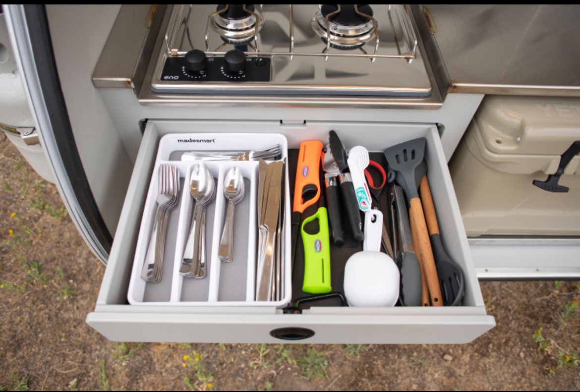 RV rental kitchen: A drawer brimming with organized utensils, cooking tools. Above, a compact stove; to the side, a cooler.