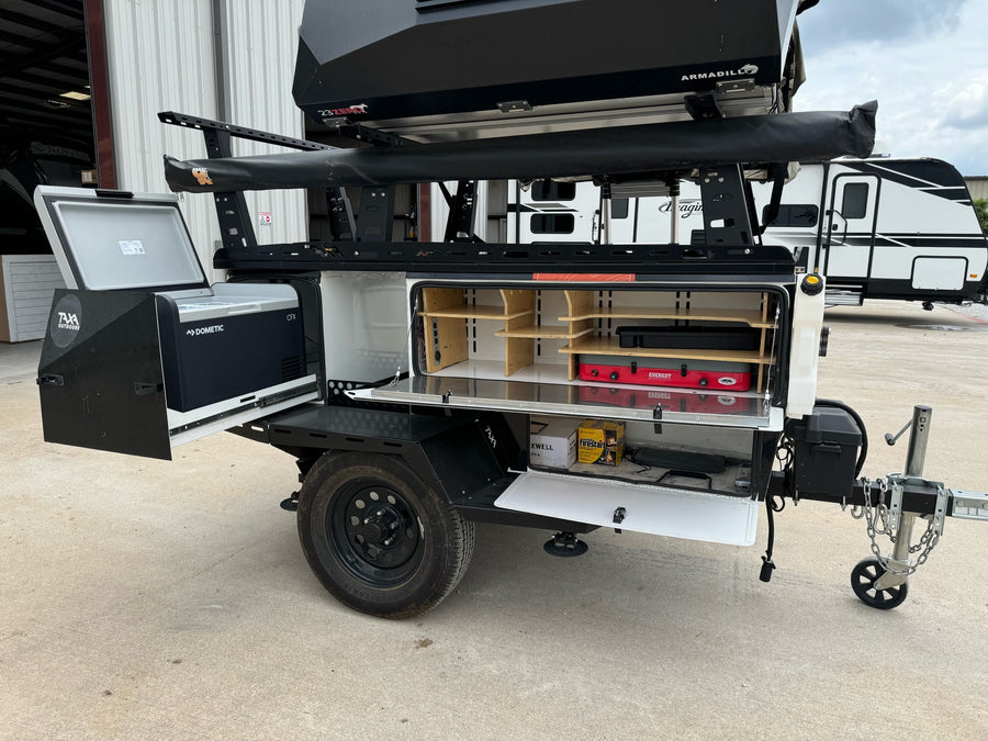 Compact RV rental trailer featuring an open outdoor kitchen with Dometic fridge, camp stove, and rooftop tent.