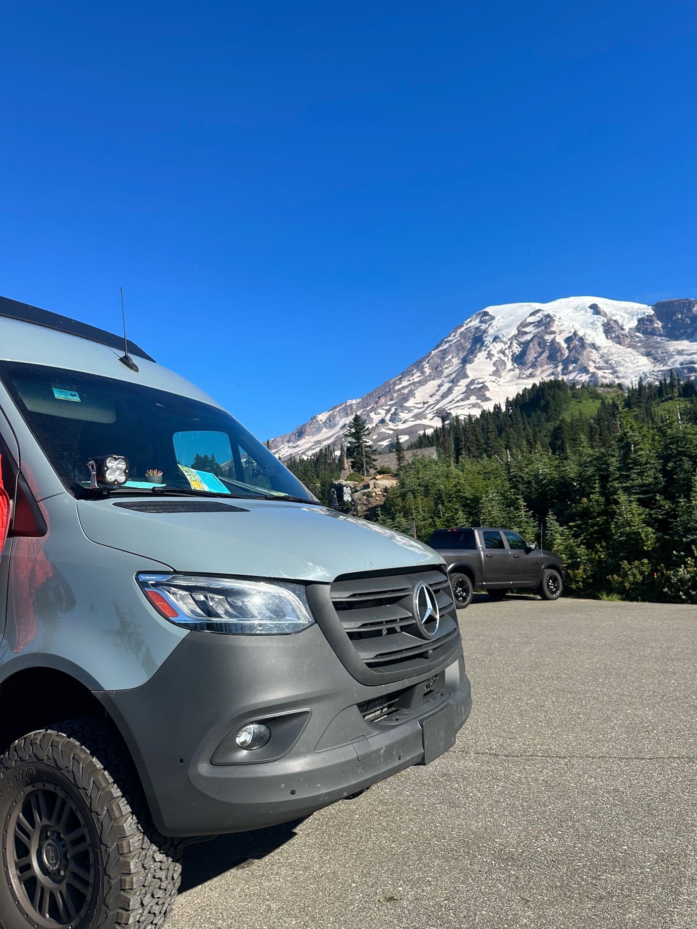 Front view of a grey Mercedes Sprinter RV rental with a majestic snow-capped mountain backdrop under a clear blue sky.