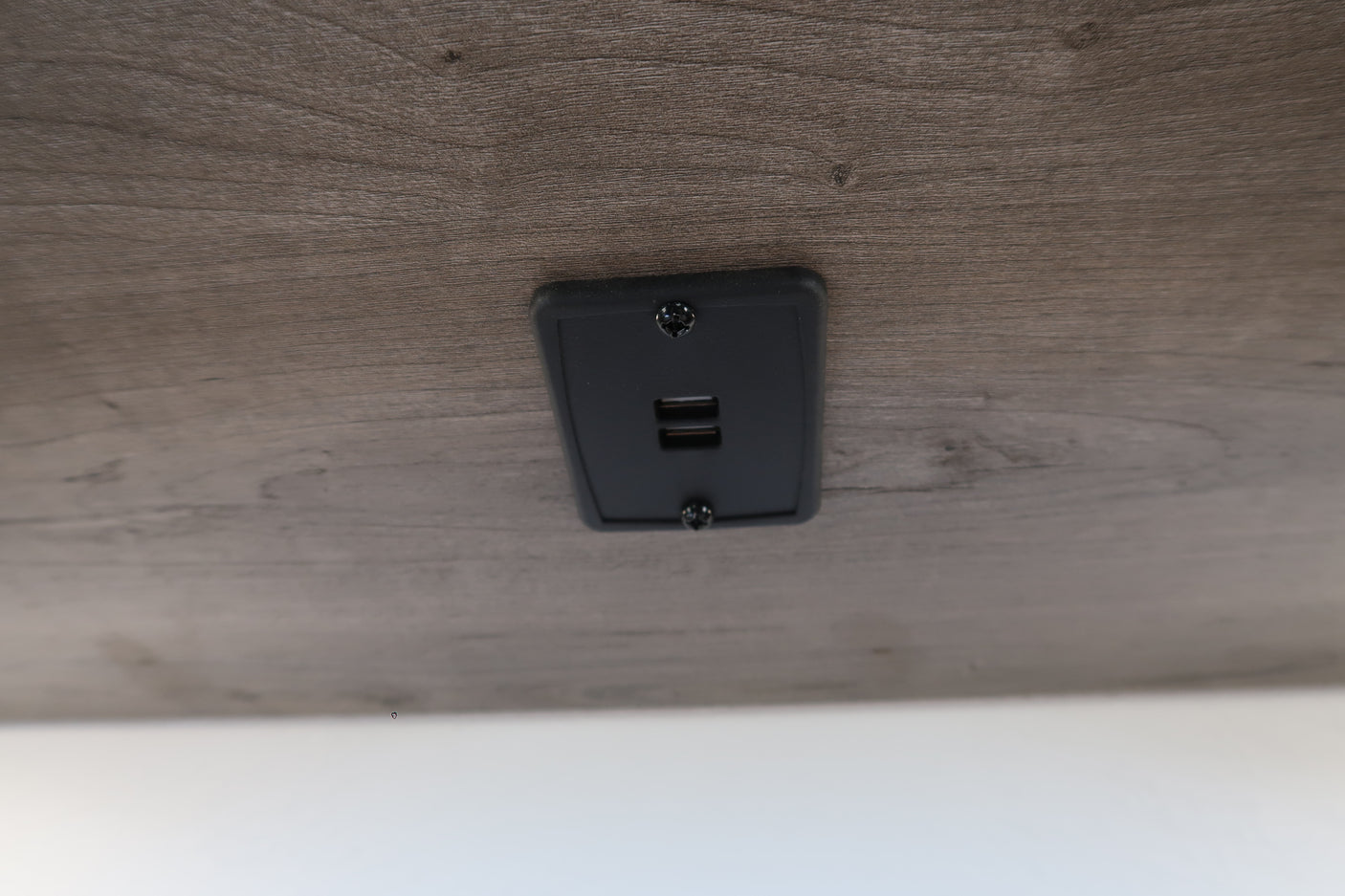 RV rental interior: Built-in USB charging station with two ports on a wood-grain surface, ideal for charging devices.