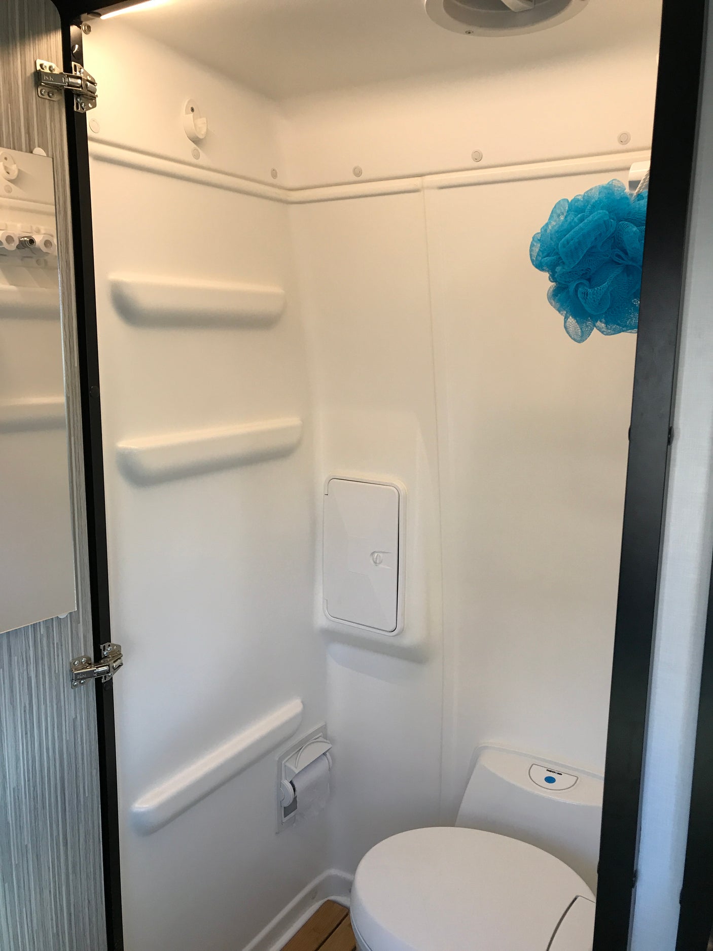 Compact white RV wet bath interior with toilet, blue loofah, and built-in features, ideal for rv rental trips.
