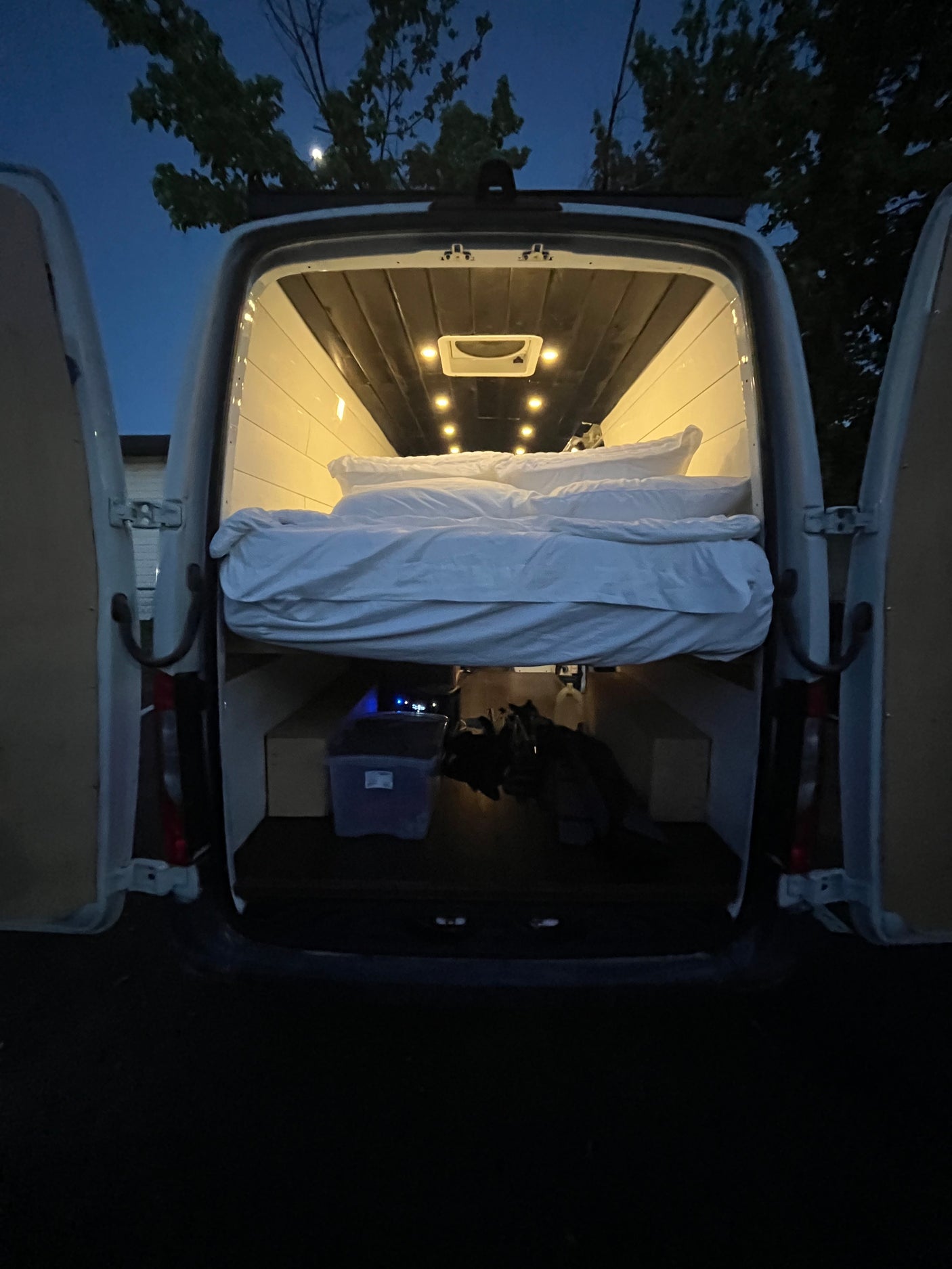 Illuminated camper van interior: a comfy raised bed above storage, ready for your next rv rental adventure.