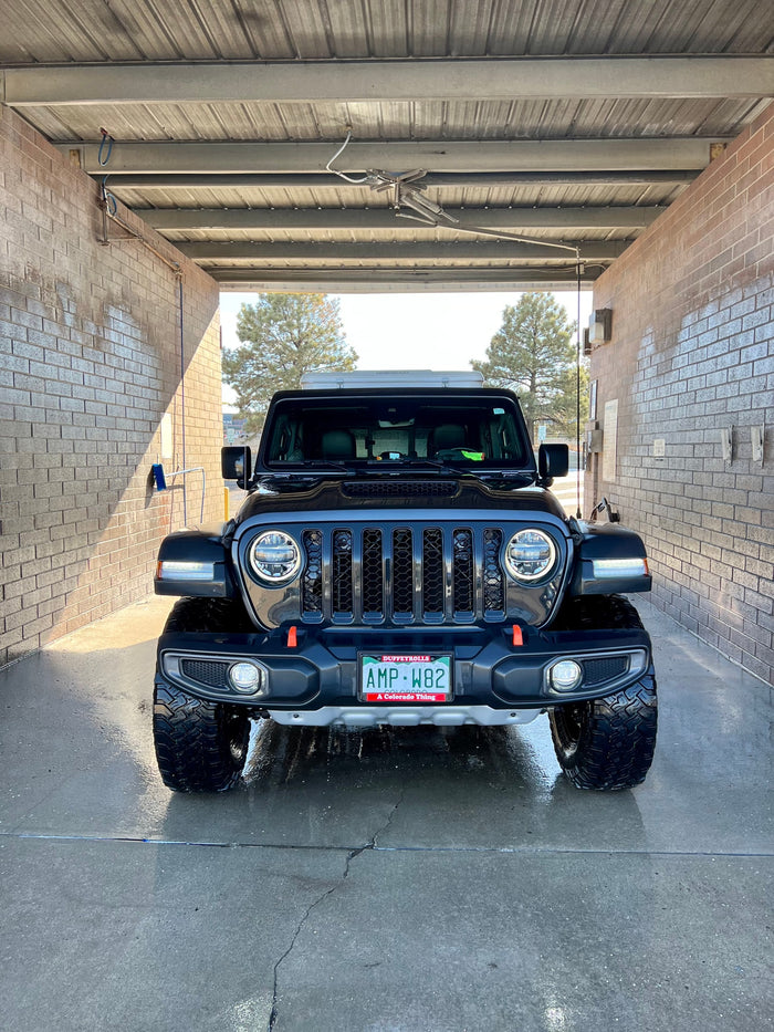 A black Jeep Gladiator with an RV rental rooftop tent, getting cleaned at a car wash, ready for Colorado adventures.