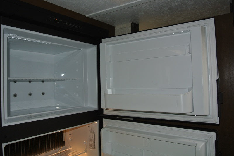 Inside a spotless RV rental refrigerator with open doors, showing freezer and fridge compartments.