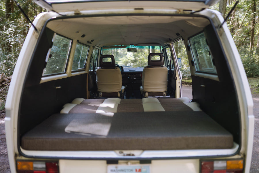 Cozy camper van interior viewed from the rear, with a bed laid out and front seats visible. Ideal for an RV rental adventure.